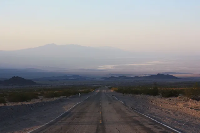 Long empty road stretching toward distant mountains at sunrise