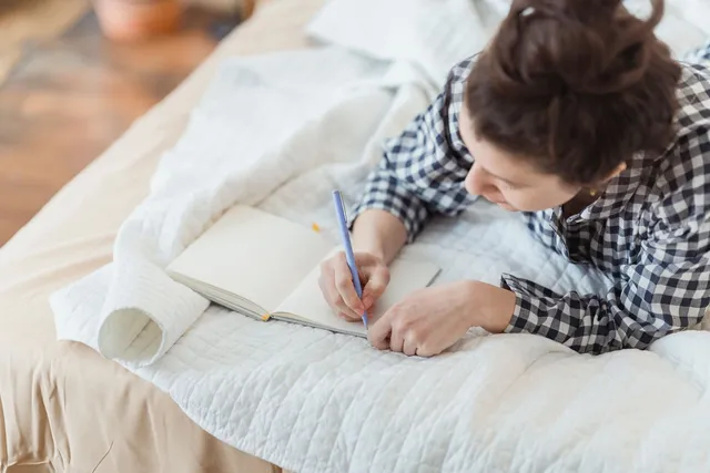 A woman writing in a journal while sitting on a cozy bed in soft light