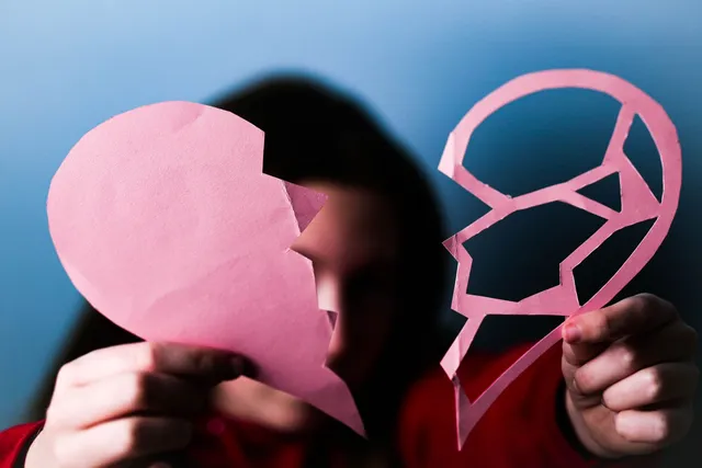 Hands holding two halves of a torn pink paper heart