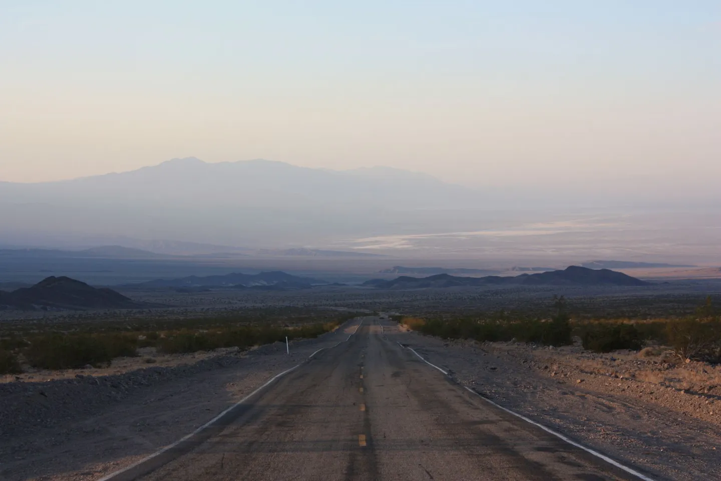 Long empty road stretching toward distant mountains at sunrise