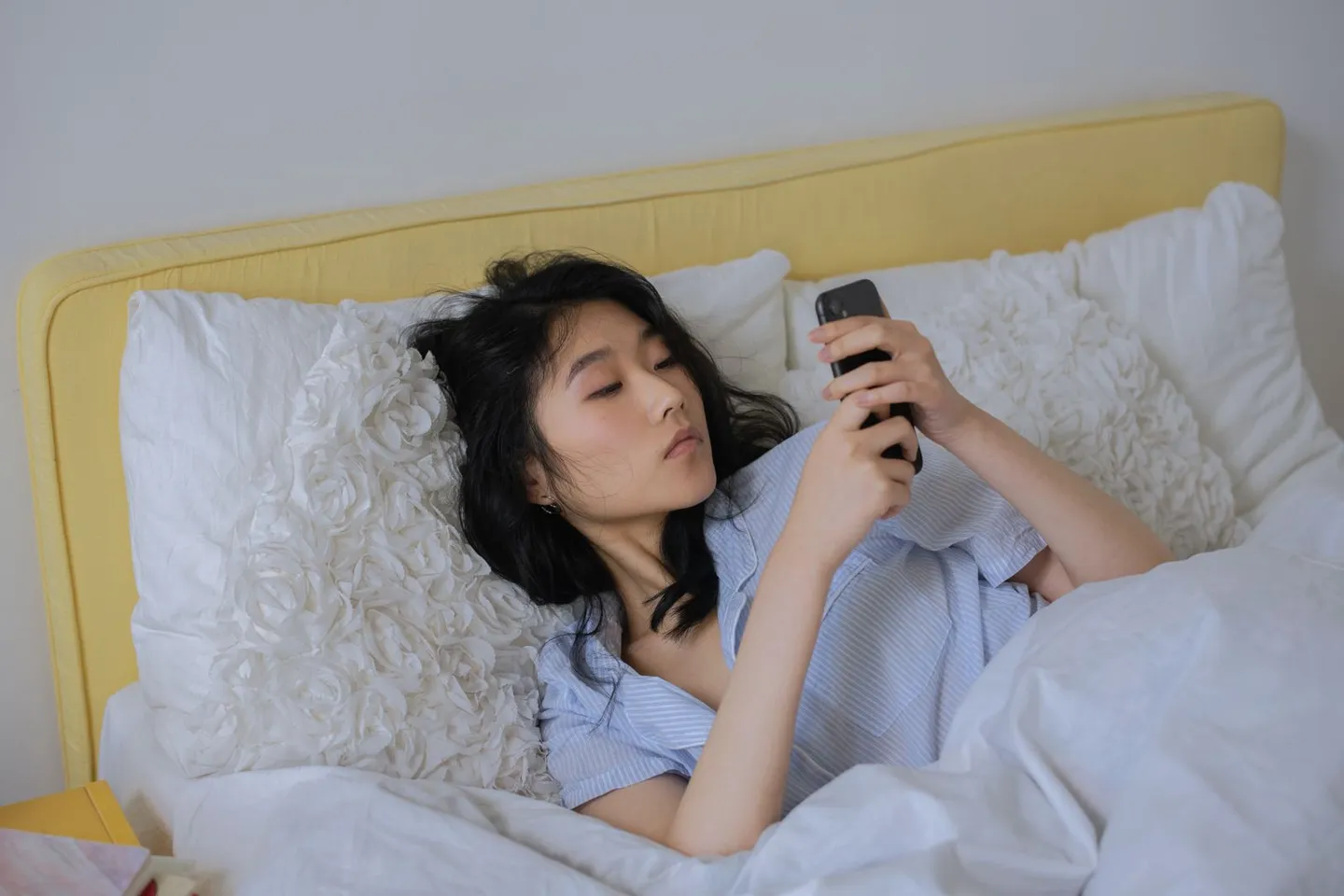 A woman lying in bed looking at her phone in a softly lit bedroom